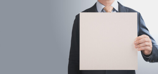 business man holding square mockup paper. man in a suit holds in his hand an empty square sheet of paper cardboard. banner. copy space