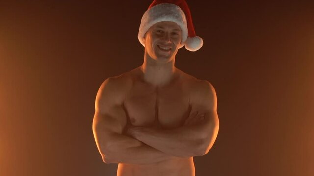 Portrait of muscular man wearing Christmas Santa hat, folded hands and smile on smoky background Macho Shirtless Naked torso stripper Hot sexy Santa guy Seductive male for holiday