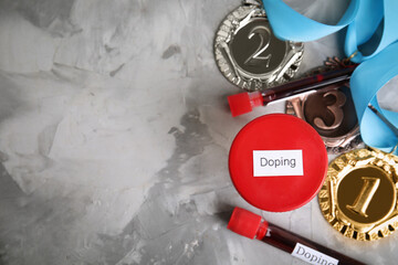 Medals, tubes of blood and urine sample with word Doping on light grey stone background, flat lay....