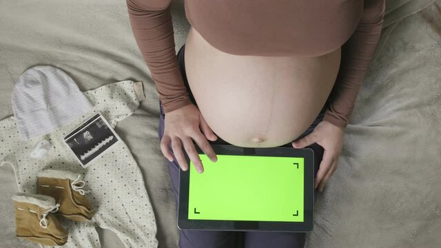expecting pregnant woman with large belly using tablet with chromakey on bed