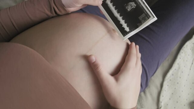 expecting pregnant woman with large belly looking at ultrasound scan at home