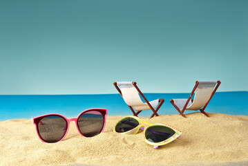 Pink glasses on the sand close up. Glasses on a beach chair background. Beach chairs on a background of blue water and sky. Summer, sea and vacation concept.