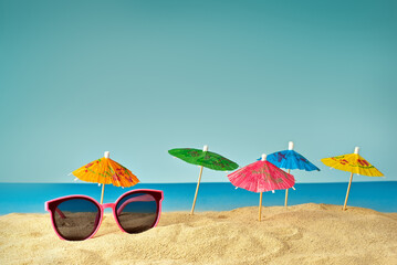 Pink glasses on the sand close up. Glasses on the beach on a background of paper umbrellas for cocktails. Summer, sea and vacation concept.