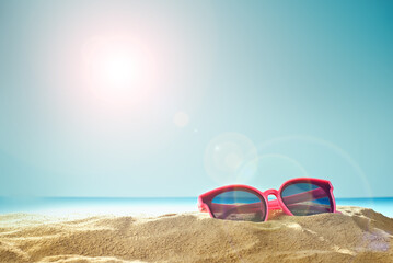 Pink glasses on the sand close up. Glasses on the beach on a background of blue water. Summer, sea and vacation concept.