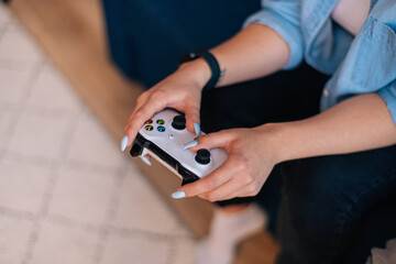 Close-up hands of unrecognizable young woman holding joystick and playing video games on console at home with friends. Closeup top view of lady gamer pressing buttons on gamepad.