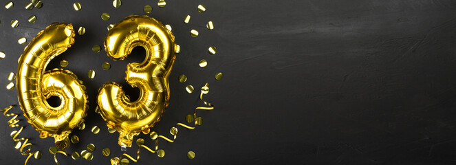 gold foil balloon number sixty three. Birthday or anniversary card with the inscription 63. Black concrete background. Anniversary celebration. Banner.