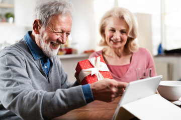 Senior couple having video call. Happy husband giving his wife a gift