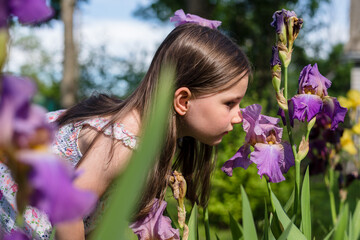 Little girl with purple irises in the garden on a sunny day. Spring and summer concept