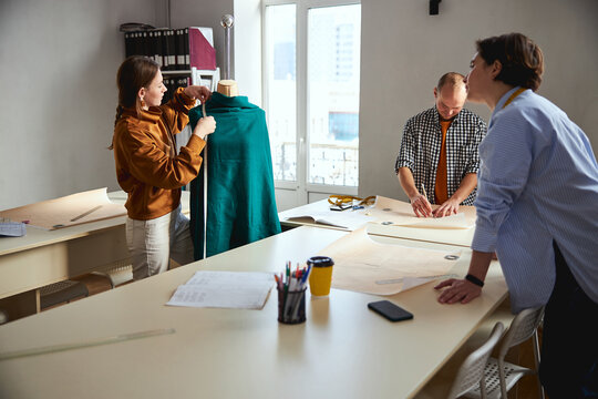 Woman taking measurements of green dress on tailor bust