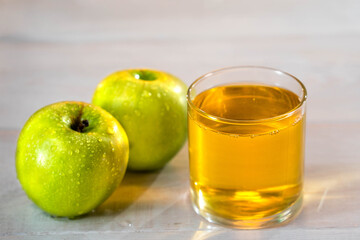 One glass of apple juice with green apples in the sunset background. Nice white wood table. Summer day. Good mood.