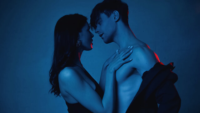 side view of woman looking at seductive boyfriend taking off blazer on blue