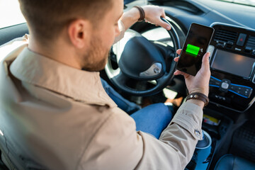 Man watching electric car charge indicator through smartphone app. Battery level on the mobile phone screen