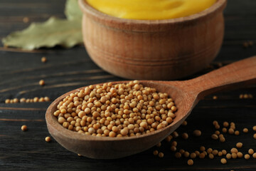 Bowl with mustard and spoon with seeds on wooden background
