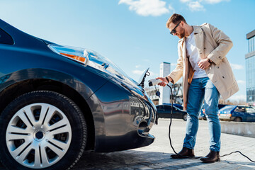 Stylish man in sunglasses inserts the charging cable into the socket of electric car