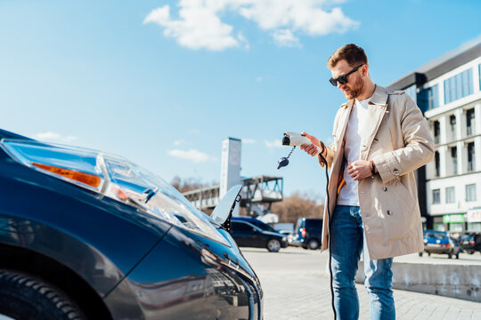 Casual Man Holds Cable For Charging Electric Car In His Hand