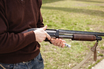 A man charges a pump-action shotgun with a Ammo. 12 caliber. Tyre outdoor. A man in headphones and goggles is preparing to shoot. Firearms for sports shooting, hobby. close up