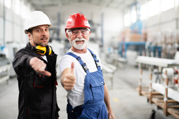 Portrait of workers in factory. Colleagues with helmet showing thumbs up.