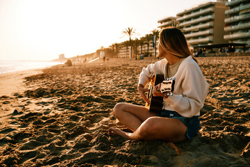 a young woman at the beach at sunset playing guitar alone