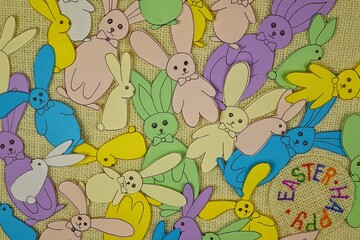 Multicolored Easter bunnies from colored paper on a white burlap, background