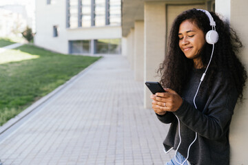 Beautiful afro girl in her 20's listening to music with her headphones in the street. space for copy space. horizontal photograph of an afro american woman relaxing listening to music.