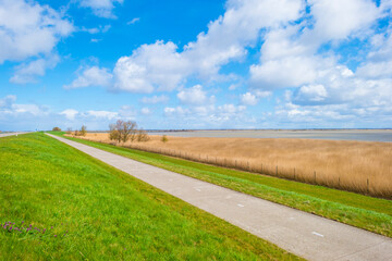 Fototapeta na wymiar Road on a dike defying a stormy lake below a blue sky and white gray clouds in spring, Almere, Flevoland, The Netherlands, April 5, 2021 