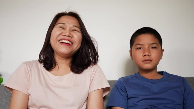slow motion scene group of asian family mother and son sitting in front of television and watching comedy movies or content together for happy lifestyle  concept