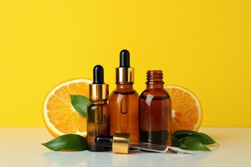 Dropper bottles with oil and oranges against yellow background