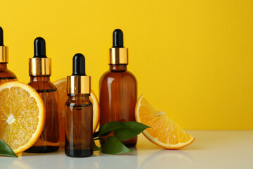 Dropper bottles with oil and oranges against yellow background