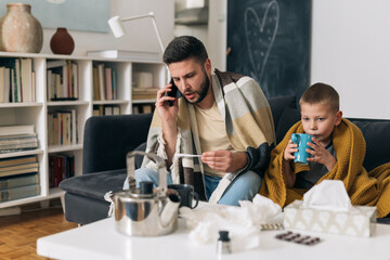 father and son have flue. they are sitting in living room blowing noses and drinking tea