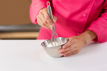 Girl baker, pastry chef, cook prepares dough for baking. Woman stirring dough in stainless
bowl with a whisk.