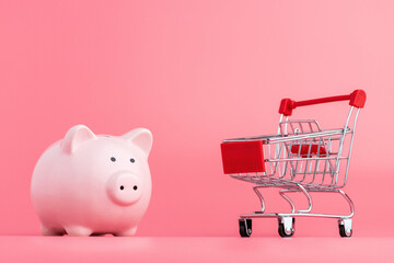 Pink piggy Bank with a shopping cart stands on a pink background. Online business shopping concept