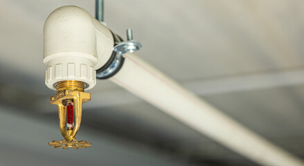 Close up image of fire sprinkler with fire in background. Fire sprinklers are part of an integrated water piping system designed for life and fire safety. - obrazy, fototapety, plakaty