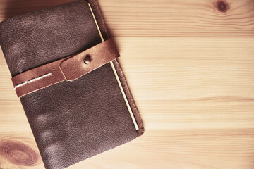 Brown leather notebook with a strap on a wooden table. Space for lettering and design