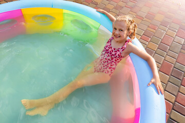 Cute adorable playful caucasian blond kid girl enjoy having fun swimming and relaxing in small inflatable pool at house garden yard on hot summer day. Children outdoor healthy acivities