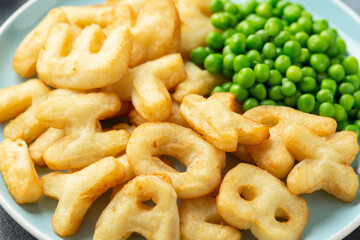 Letters potato fries snack with green peas and ketchup on plate. party food