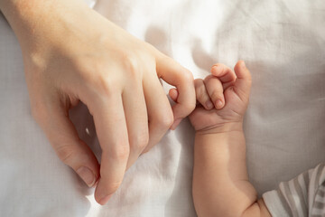 Mother Baby Connection. Newborn child holding mom's hand while lying in bed