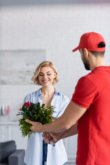 young arabian courier holding bouquet near pretty woman, blurred foreground