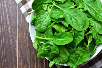  Fresh spinach leaves in a white bowl, on a plaid cloth. 