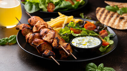 Chicken fillet souvlaki, kebabs on skewers with potato chips, salad and fresh home made tzatziki