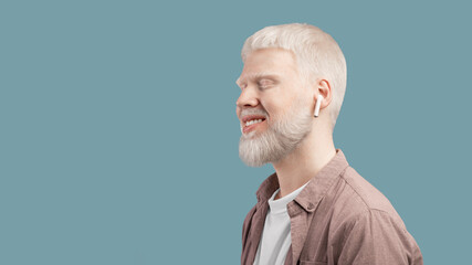 Relaxed albino man listening music in wireless airpods earphones on turquoise background, panorama with free space - obrazy, fototapety, plakaty