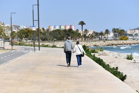 An elder couple walking on a pathway nearby the beach of Villajoyosa-Spain.