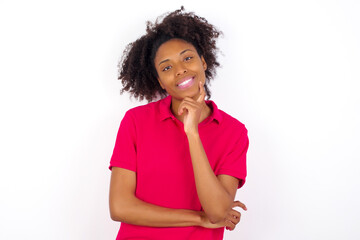 Cheerful young beautiful African American woman wearing pink t-shirt against white wall with hand near face. Looking with glad expression at the camera after listening to good news. Confidence.