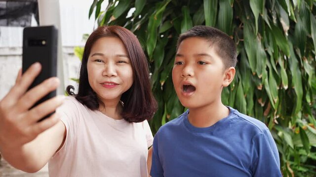 slow motion scene of mother and son holding smartphone to video call with family or relatives   at outside home garden during quarantine lockdown period for lifestyle concept
