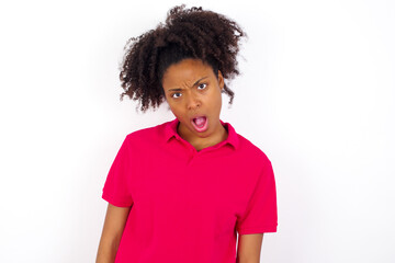 Fototapeta na wymiar Expressive facial expressions. Shocked stupefied young beautiful African American woman wearing pink t-shirt against white wall, keeps jaw dropped feels stunned from what he sees aside.