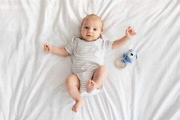 Adorable newborn baby wearing bodysuit lying on bed and looking at camera