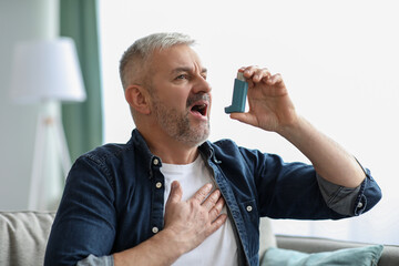Senior man touching chest and using inhaler