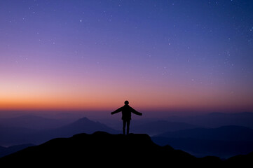 Silhouette of happy woman open hands against and watched night sky, star and milky way background alone on top of the mountain. People having fun on summer vacation  freedom and imagination concept.