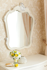 Elegant white commode with beautiful mirror and yellow wedding bouquet on it