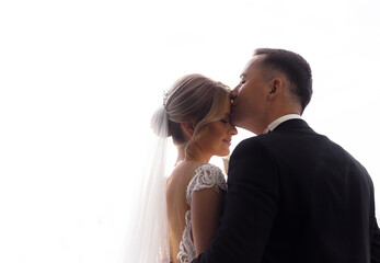 Back view of young groom hugs and kisses his beautiful bride on a white background. Concept of wedding couple