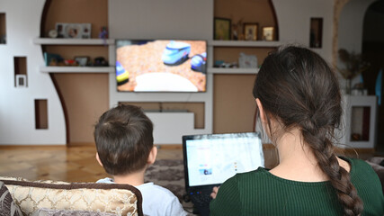 Young mother works at laptop while son watches cartoons. Working mom concept